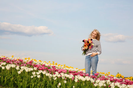 Happy woman with spring bouquet of flowers in beautiful tulip field on sunny dayの写真素材