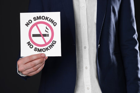 Woman holding card with no smoking sign on black background, closeupの写真素材