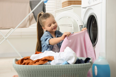 Little girl taking out dirty clothes from basket in bathroomの写真素材