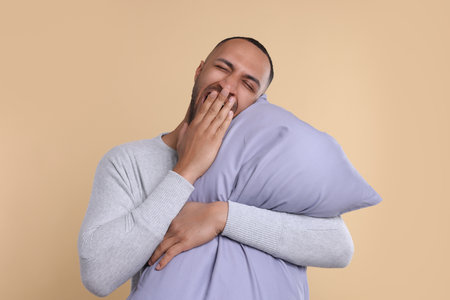 Sleepy man with pillow yawning on beige background. Insomnia problemの写真素材