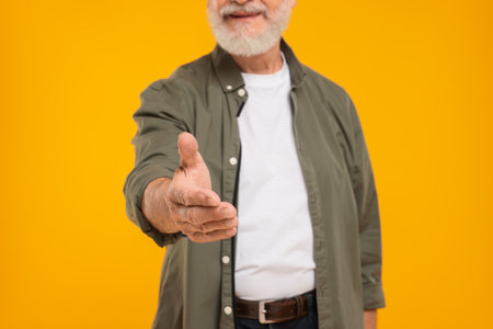 Man welcoming and offering handshake on yellow background, closeup