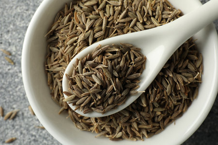 Caraway (Persian cumin) seeds and spoon in bowl on gray table, top view