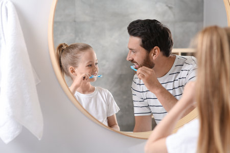 Father and his daughter brushing teeth together near mirror in bathroomの写真素材