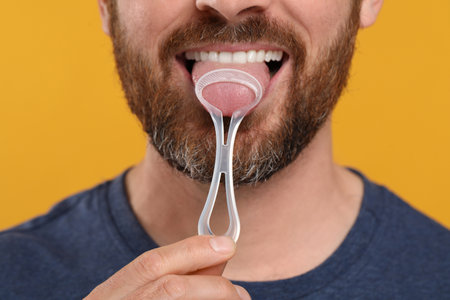 Man brushing his tongue with cleaner on yellow background, closeupの写真素材