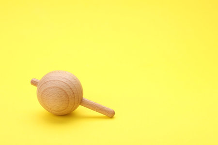 One wooden spinning top on yellow background, space for text. Toy whirligigの写真素材
