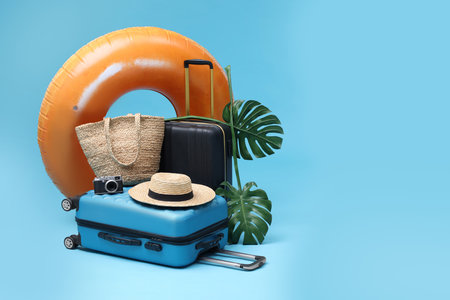 Suitcases, beach accessories and tropical leaves on light blue background, space for text. Summer vacationの写真素材