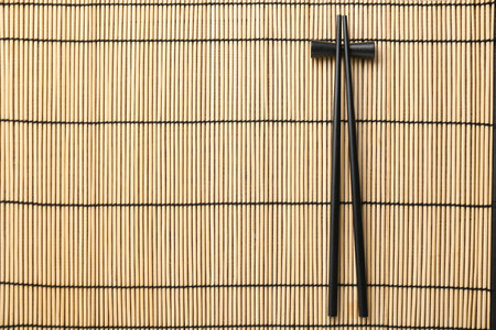 Pair of black chopsticks with rest on bamboo mat, top view. Space for textの写真素材