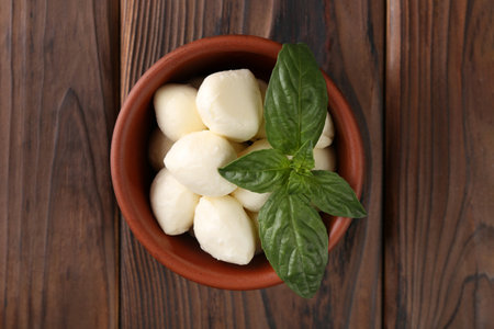 Tasty mozarella balls and basil leaves in bowl on wooden table, top viewの写真素材