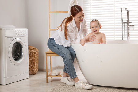 Mother washing her little baby in tub at home