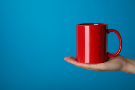 Woman holding red mug on light blue background, closeup. Space for textの写真素材