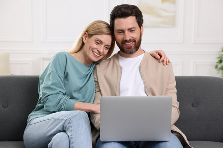 Happy couple with laptop on sofa at homeの写真素材