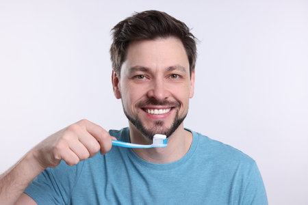 Happy man holding plastic toothbrush on white background. Mouth hygiene