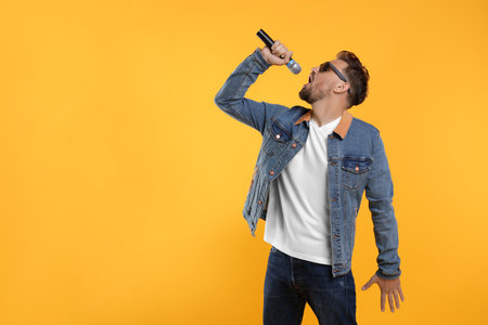 Handsome man with sunglasses and microphone singing on yellow background. Space for textの写真素材