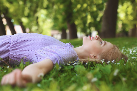 Beautiful woman lying on green grass in park. Spring sunny dayの写真素材