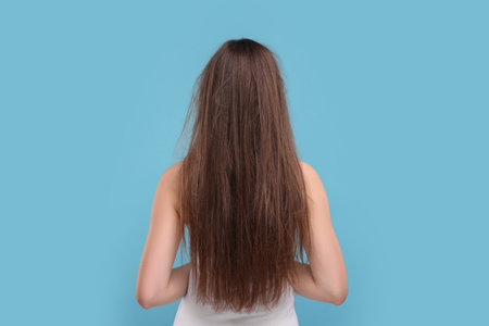 Woman with damaged messy hair on light blue background, back viewの写真素材
