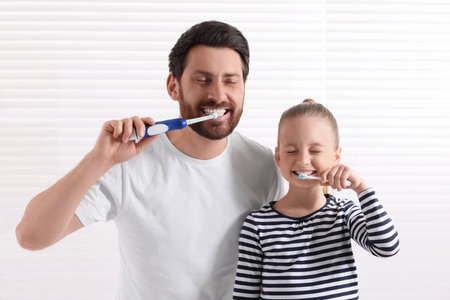 Father and his daughter brushing teeth together in bathroomの写真素材