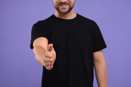 Man welcoming and offering handshake on purple background, closeupの写真素材