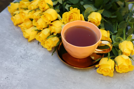 Cup of tea and beautiful yellow roses on light table, space for textの写真素材
