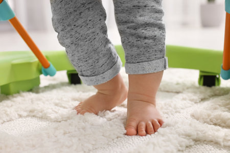 Little baby taking first steps with toy walker on carpet indoors, closeupの写真素材