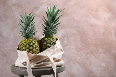 Bag with delicious ripe pineapples on stand against pink wall. Space for textの写真素材