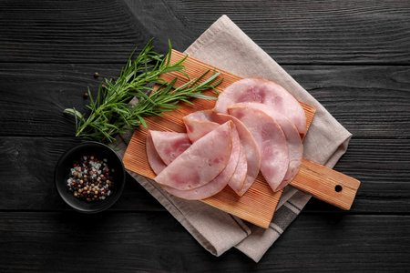 Slices of delicious ham with rosemary and spices on dark wooden table, flat lay