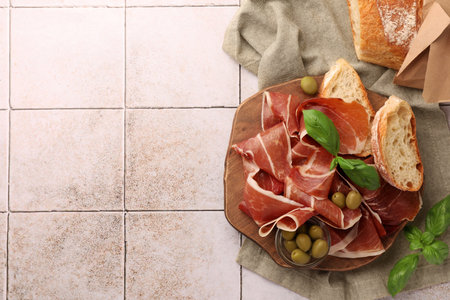 Slices of tasty cured ham, olives, bread and basil on tiled table, flat lay. Space for textの写真素材