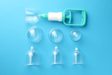 Plastic cups and hand pump on light blue background, flat lay. Cupping therapyの写真素材