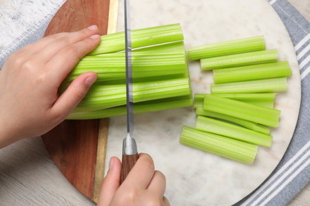 Woman cutting fresh green celery at white table, top view