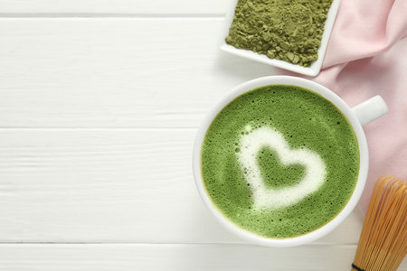 Cup of fresh matcha latte, powder and bamboo whiskey on white wooden table, flat lay. Space for textの写真素材