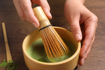 Woman preparing matcha tea at wooden table, closeup