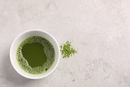 Cup of matcha tea on light gray textured table, top view. Space for text