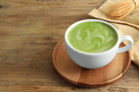 Cup of aromatic matcha latte on wooden table. Space for text