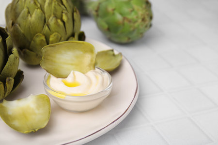 Delicious cooked artichokes with tasty sauce served on white tiled table, closeup. Space for textの写真素材