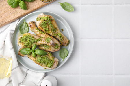 Delicious fried chicken drumsticks with pesto sauce and ingredients on white tiled table, flat lay. Space for textの写真素材