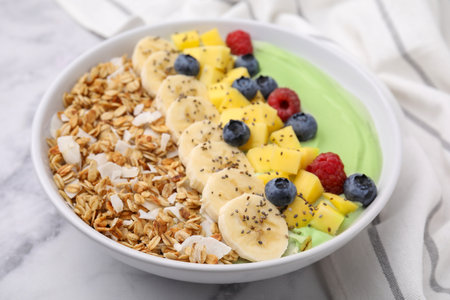 Tasty matcha smoothie bowl served with fresh fruits and oatmeal on white marble table, closeup. Healthy breakfastの写真素材