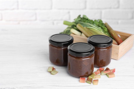 Jars of tasty rhubarb jam and cut stalks on white wooden table, space for textの写真素材