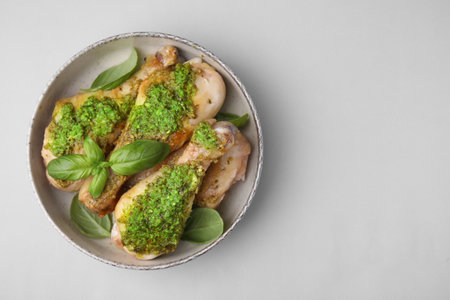 Delicious fried chicken drumsticks with pesto sauce and basil in bowl on light gray table, top view. Space for textの写真素材