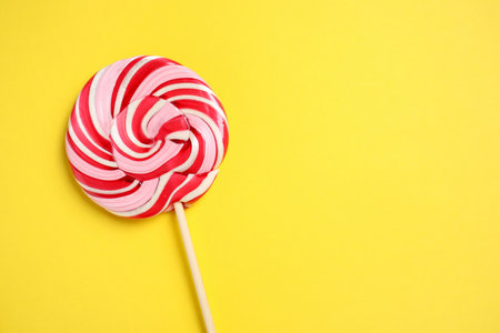 Stick with colorful lollipop swirl on yellow background, top view. Space for textの写真素材