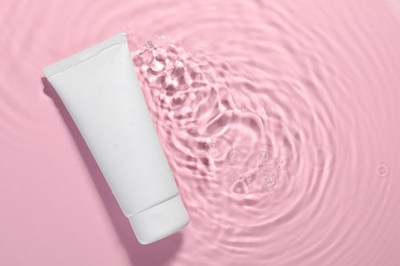 Tube of facial cleanser in water against pink background, top view. Space for text