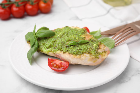 Delicious chicken breast with pesto sauce, tomato and cutlery served on white table, closeupの写真素材