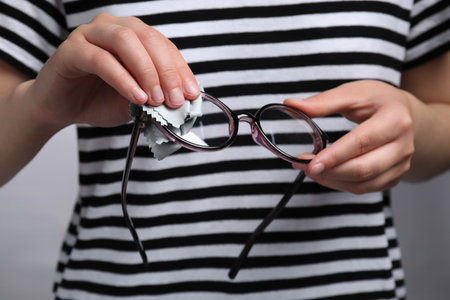 Woman wiping glasses with microfiber cloth on light gray background, closeupの写真素材