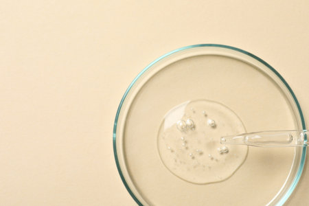 Petri dish with sample of cosmetic oil on beige background, top view. Space for textの写真素材