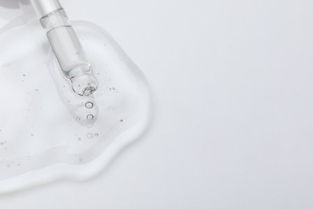Dripping cosmetic oil from pipette onto light surface, closeup. Space for textの写真素材