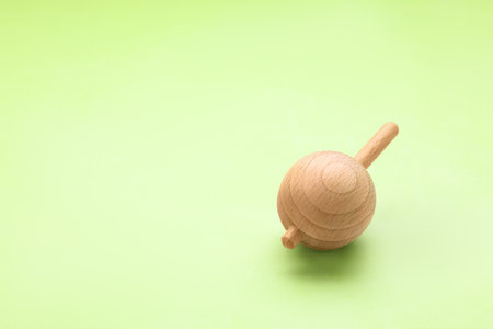 One wooden spinning top on light green background, space for text. Toy whirligigの写真素材