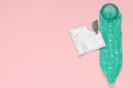 Unrolled condom and torn package on pink background, top view with space for text. Safe sexの写真素材