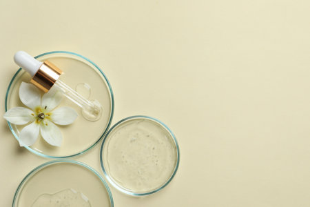 Petri dishes with samples of cosmetic oil, pipette and beautiful flower on beige background, flat lay. Space for textの写真素材