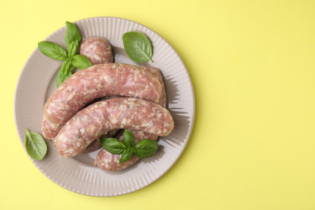 Raw homemade sausages and basil leaves on yellow background, top view. Space for textの写真素材