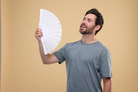Man with hand fan suffering from heat on beige backgroundの写真素材