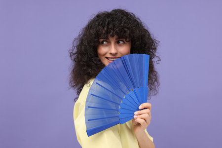 Happy woman holding hand fan on purple backgroundの写真素材