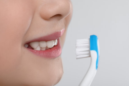 Girl brushing her teeth with toothbrush on light gray background, closeupの写真素材